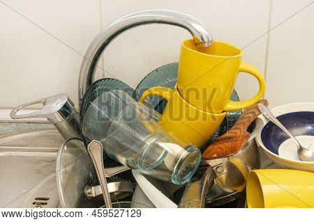 Dirty And Unwashed Dishes Are Stacked In The Kitchen Sink. Unwashed Cups, Plates, Pots, Forks And Sp