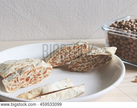 Front View Of Raw Tempeh Or Tempe. Tempeh Slices In White Ceramic Plate And Bowl Of Dry Soybean Seed