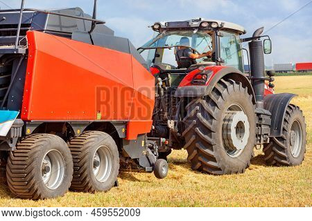 A Tractor With A Large Red Two-axle Trailer For Harvesting Against The Background Of A Harvested Whe