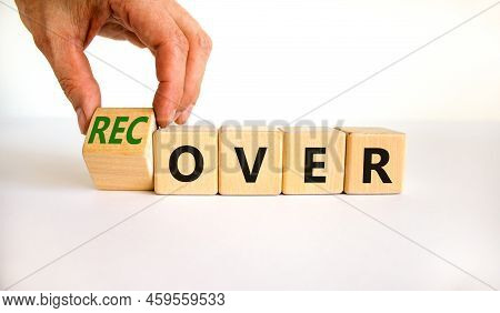 Time To Recover Symbol. Businessman Turns A Wooden Cube And Changes The Word 'over' To 'recover'. Be