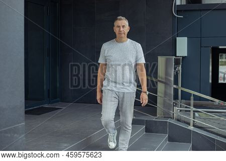 Portrait Of Confident Aged Gray Haired Businessman Going Along Stairs Near Entrance Of Gray Modern O