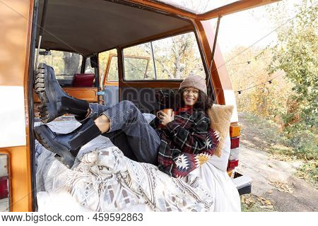 Young African American Woman Sitting At Table Near Car In Autumn Forest And Drinking Hot Tea, Dreamy