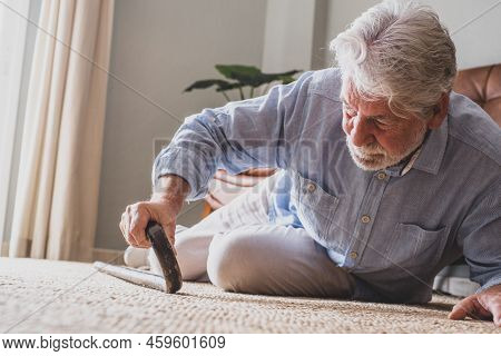 Elder Senior Man Lying On Floor After Falling Down With Wooden Walking Stick Beside Couch On Rug In 