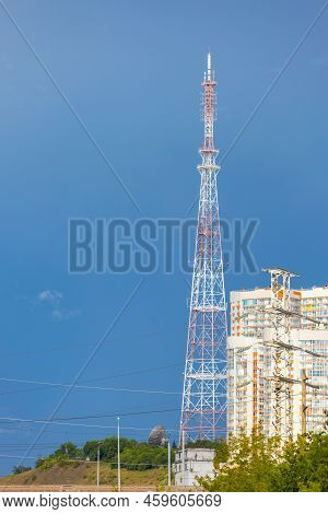 Red And White Communication Tower Against The Blue Sky. Tele-radio Tower Next To Residential Apartme