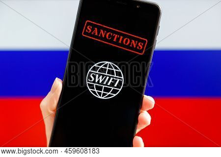Ukraine, Kiev - February, 23 2022: Hand Holding Mobile With Swift Logo, Sanctions And Russian Flag I