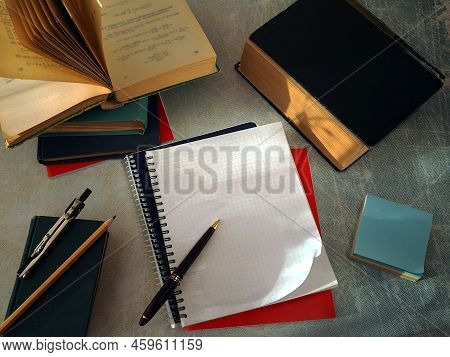Open Books And Notebooks Lie On The Table. There Is A Pen On A Clean Notebook Page. The Concept Of E
