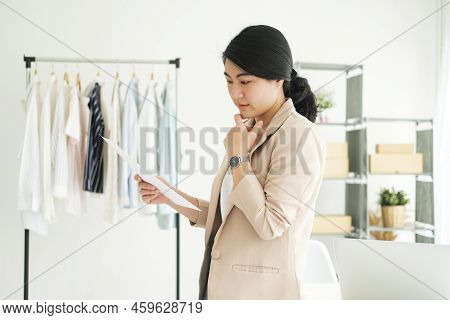 Young Asian Female Freelan Standing Reading Report On Paper In Online Clothing Store.