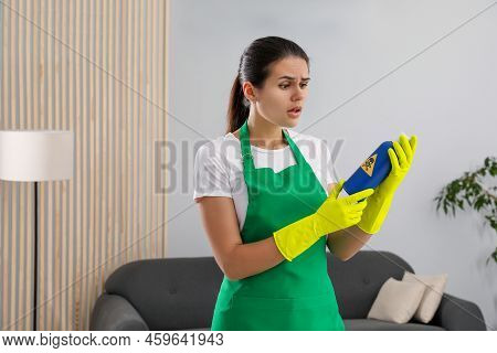 Woman Looking At Bottle Of Toxic Household Chemical With Warning Sign Indoors