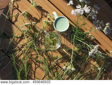 Yarrow Plants And Glass Of Yarrow Herb Tea On Wooden Table, Top View.