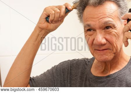 Mature Man 60plus Combing His Mostly Gray Hair In The Back Of His Head In Front Of A Mirror
