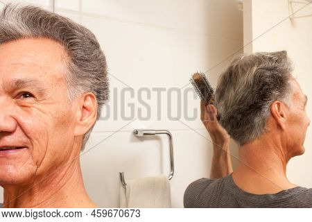 Mature Man 60plus Combing His Mostly Gray Hair In The Back Of His Head In Front Of A Mirror
