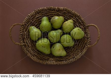 Top View Of Green Barlett Pears In The Brown Woven Backet On Terracotta Background.
