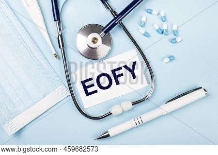 On A Blue Background, A Stethoscope, A Medical Mask, Pills, A Pen And A White Card With The Text Eof