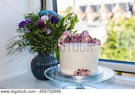 Birthdag Cake Decorated With Pink Flowers And A Bouguet Of Flowers In A Vase On The Windowsill.