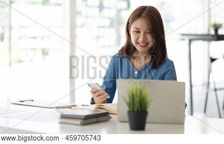 Smiling Pretty Girl Working On Laptop Computer While Sitting At Office Table, Taking Notes In A Diar