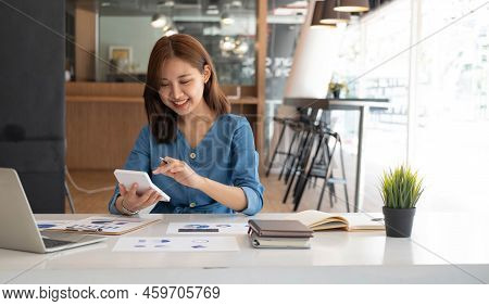 Smiling Pretty Girl Working On Laptop Computer While Sitting At Office Table, Taking Notes In A Diar