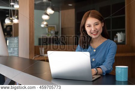Smiling Pretty Girl Working On Laptop Computer While Sitting At Office Table, Taking Notes In A Diar