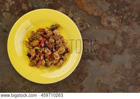 Yakisoba With Chicken Meat On A Yellow Plate On A Rusty Slate Stone - Top View