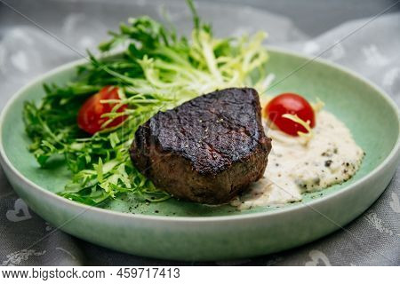 Culinary Mistake. A Piece Of Overcooked And Burnt Beef Meat On Salad Leaves With Cherry Tomatoes And