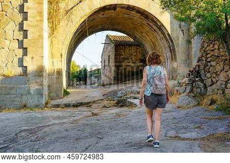 Tourist Woman Crossing An Old Stone Bridge At The Entrance Of A Village In Castile, Puente Congosto.
