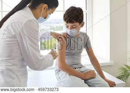 Nurse Or Doctor At Clinic Giving Vaccine To Little School Child In Medical Face Mask