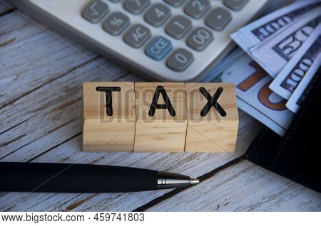 Tax Word On Wooden Blocks With Calculator And Bank Notes Background. Tax Concept.