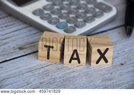 Tax Word On Wooden Blocks With Calculator Background. Tax Concept.