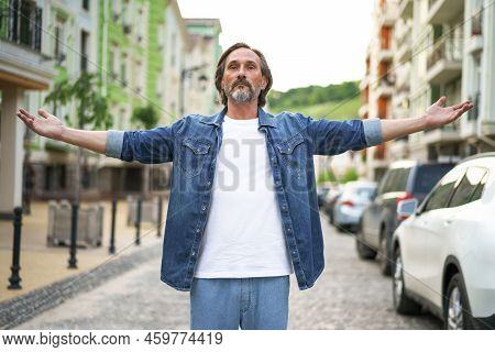 Happy Senior Man Thanks God Standing Outdoors With Hands Spread Wide Open Wearing Jeans Shirt With W