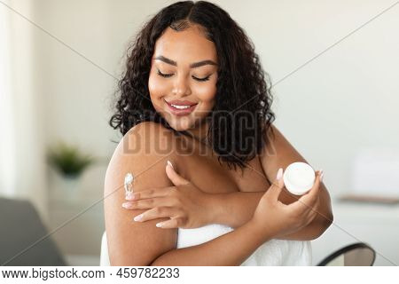 Young African American Chubby Woman Applying Skin Butter Or Mosturizer On Her Shoulder After Morning