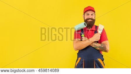 Happy Bearded Man Housepainter In Work Clothes Hold Paint Roller And Brush On Yellow Background