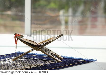 Rehal With Open Quran And Misbaha On Muslim Prayer Rug Near Window Indoors, Space For Text
