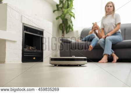 Cute Child Near Mother Looking At Robotic Vacuum Cleaner In Living Room