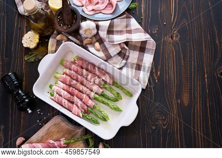 Ceramic Baking Dish With Aspargus Covered With Bacon On Wooden Kitchen Table
