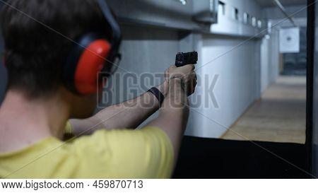 Close-up Of Male Shooter In Headphones Aiming Pistol At Target In Shooting Range. Shooting Practicin