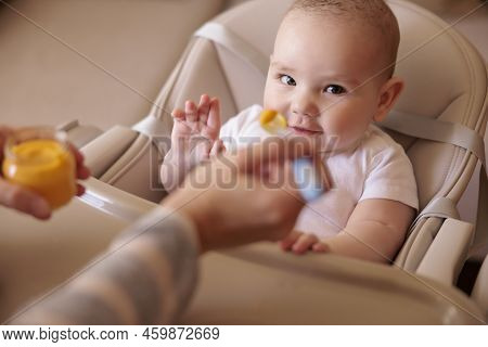 Mother Feeding Porridge To Her Happy Cheerful Baby Boy Using Spoon, Cheerful And Happy Baby Sitting 