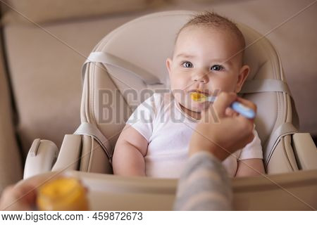 Mother Feeding Porridge To Her Happy Cheerful Baby Boy Using Spoon, Cheerful And Happy Baby Sitting 