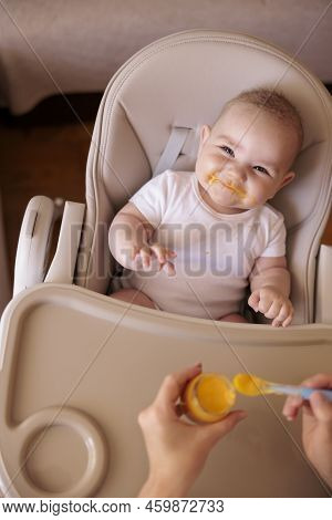 High Angle View Of Mother Feeding Cheerful Baby Boy With Porridge, Baby Sitting In High Chair All Me