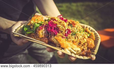 Street Food - Hand Holding Portion Of Spicy Chicken Wings With Red Cabbage And Herbs