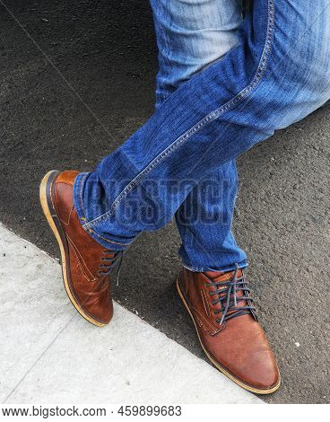 The Lower Of The Legs Of A Standing Man Wearing Blue Denim Jeans With Brown Leather Shoes.
