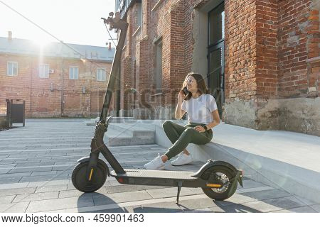Young Woman In White Sneakers Is Sitting Near Electric Scooter