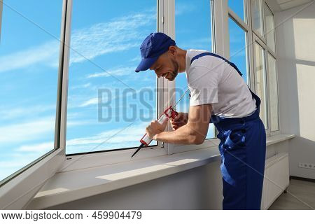 Worker Sealing Plastic Window With Caulk Indoors. Installation Process