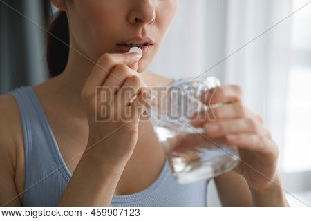 A Young Woman Takes Medications Or Vitamins. Shes Holding A Glass Of Water.