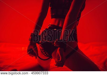 Woman With A Sexy Booty With Handcuffed Hands Sits Erotically On Bed In Bedroom. Bdsm Concept Of Sex