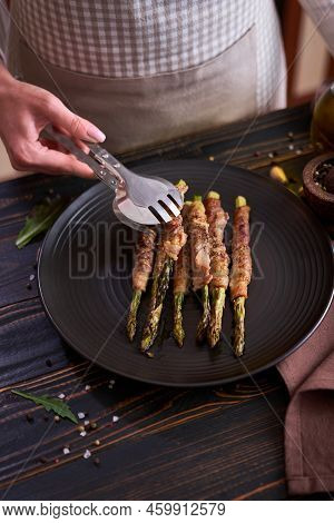 Baked Aspargus Covered With Bacon On A Black Ceramic Plate On Wooden Kitchen Table