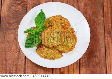Fried Small Thick Savory Pancakes Made With Grated Vegetable Marrows And Fresh Basil Leaves On White