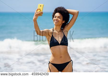 Glad Slim African American Female Tourist In Stylish Swimwear Taking Self Portrait On Cellphone Whil