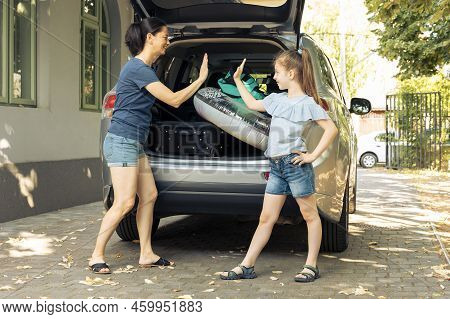 Woman And Young Child Doing Highfive Before Leaving On Holiday Trip At Seaside, Loading Baggage And 