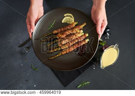 Baked Aspargus Covered With Bacon On A Black Ceramic Plate