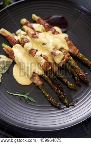 Baked Aspargus Covered With Bacon On A Black Ceramic Plate