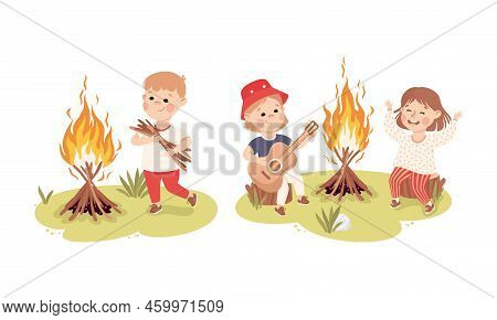 Little Children Camping Around Bonfire. Boy Carrying Bunch Of Firewood Kids Playing Guitar And Singi